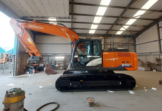 Hitachi 210LC tracked excavator parked in a machinery shed.